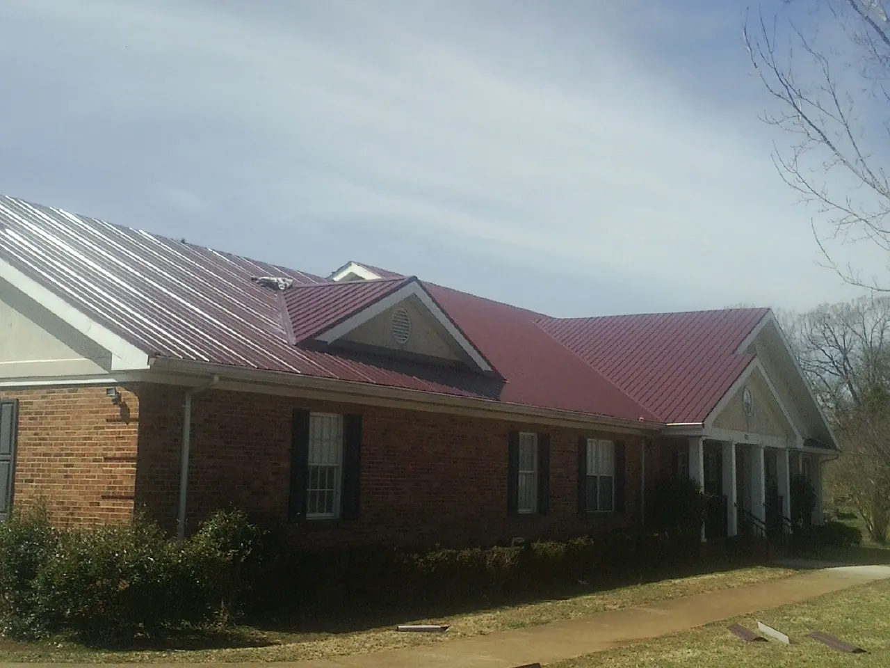 Red metal roof with gabled entries on a long brick building, from a Hail Damage Roof Repair job in Wallis