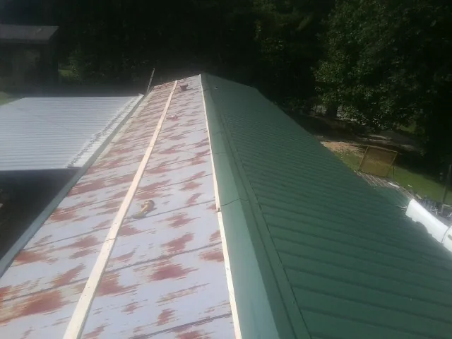 Old rusted panels beside newly installed green metal roofing — Wind Damage Roof Repair by Roofing Brothers in Wallis