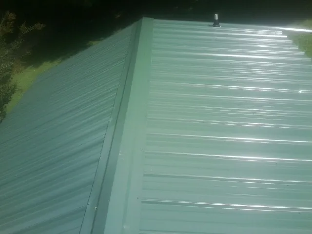 New green metal panels meeting at the ridge of a roof — Flat Roof Repair work by our crew in Wallis