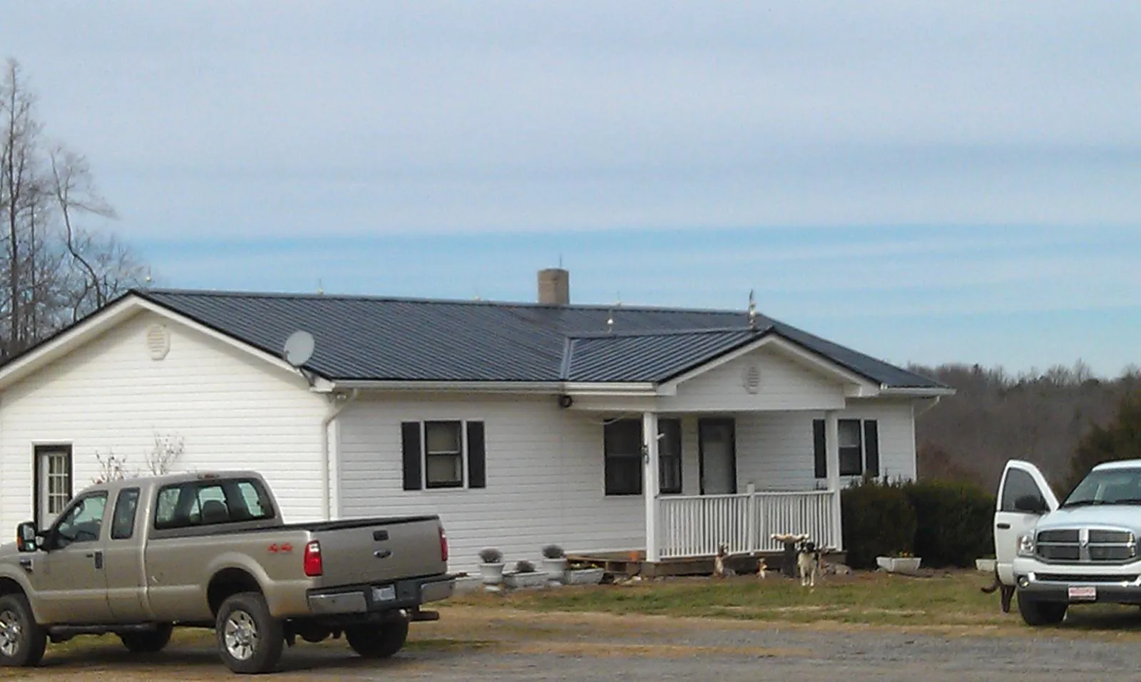 Finished dark metal roof on a white ranch home with work trucks parked in Wallis